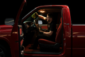Technician reaching over the dashboard to clean the interior windshield of a 1990s Dodge Ram 1500 with warm cab lighting in a dark luxury detailing studio